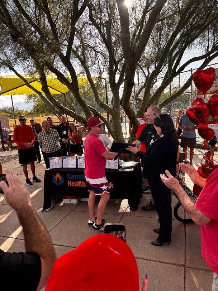 A player in a red cap accepts a framed award from Carondelet Health Network representatives as the crowd applauds.